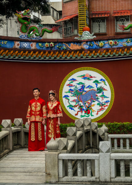 Ein Hochzeitspaar in traditioneller Kleidung steht vor einer Mauer im Konfuziustempel
